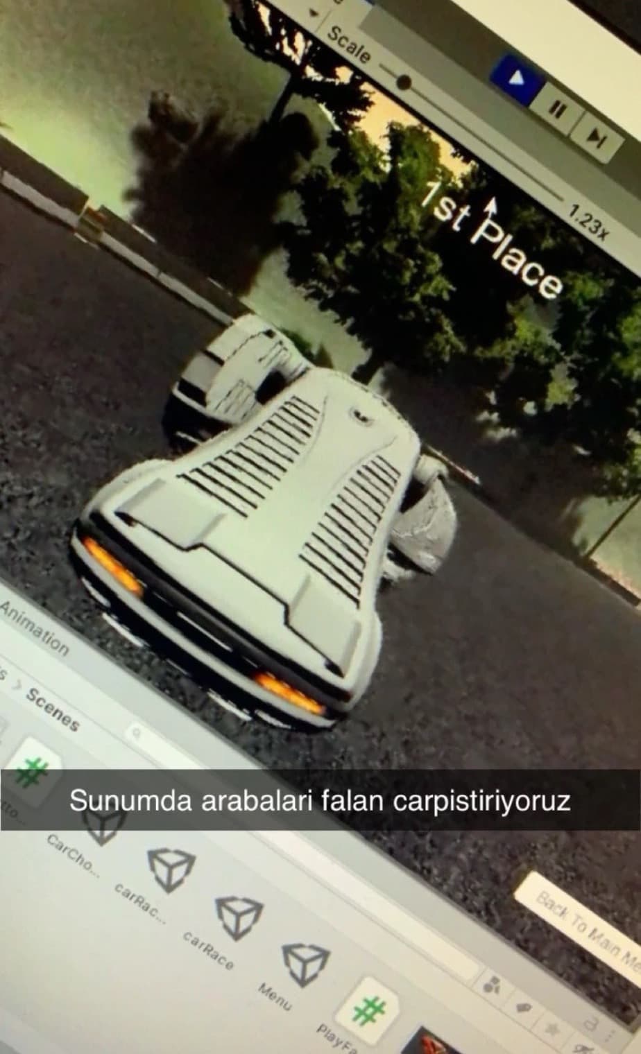 Bir bilgisayar ekranının telefonla çekilmiş fotoğrafı: Play modunda Unity editörü, arkadan görünen beyaz bir spor araba ve hemen yanında rakip bir araba, ekranda "1st Place" yazısı ve fotoğrafın üstüne yazılmış Türkçe bir not.